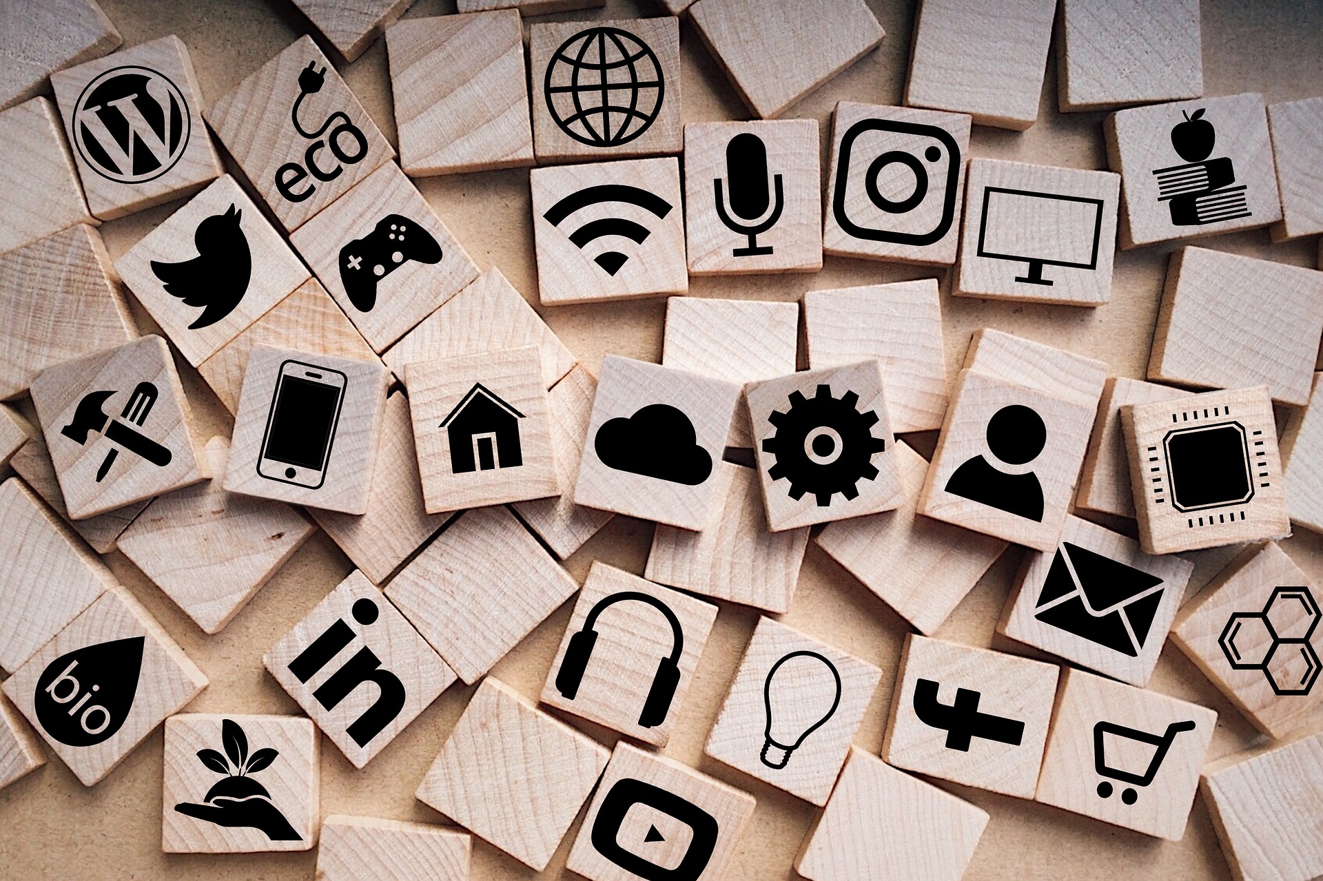 Looking down on a jumbled assortment of small, wooden tiles, each stamped with a different icon symbolizing business, social media, or communications.